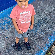 Tylan is registered to the contest to win money with this photo: child, boy, toddler, standing, outdoor, concrete, blue_wall, shirt, shorts, sneakers, expression, funny_face, hair, sidewalk, urban, casual_clothing, leaves, daylight, playful, person
