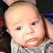 Arizona Rose joined the competition — help win amazing prizes! baby, infant, child, face, portrait, close_up, wide_eyes, looking_at_camera, neutral_expression, light_skin, short_hair, blanket, clothing, adult_hand, indoor, cozy, head, eyes, nose, mouth