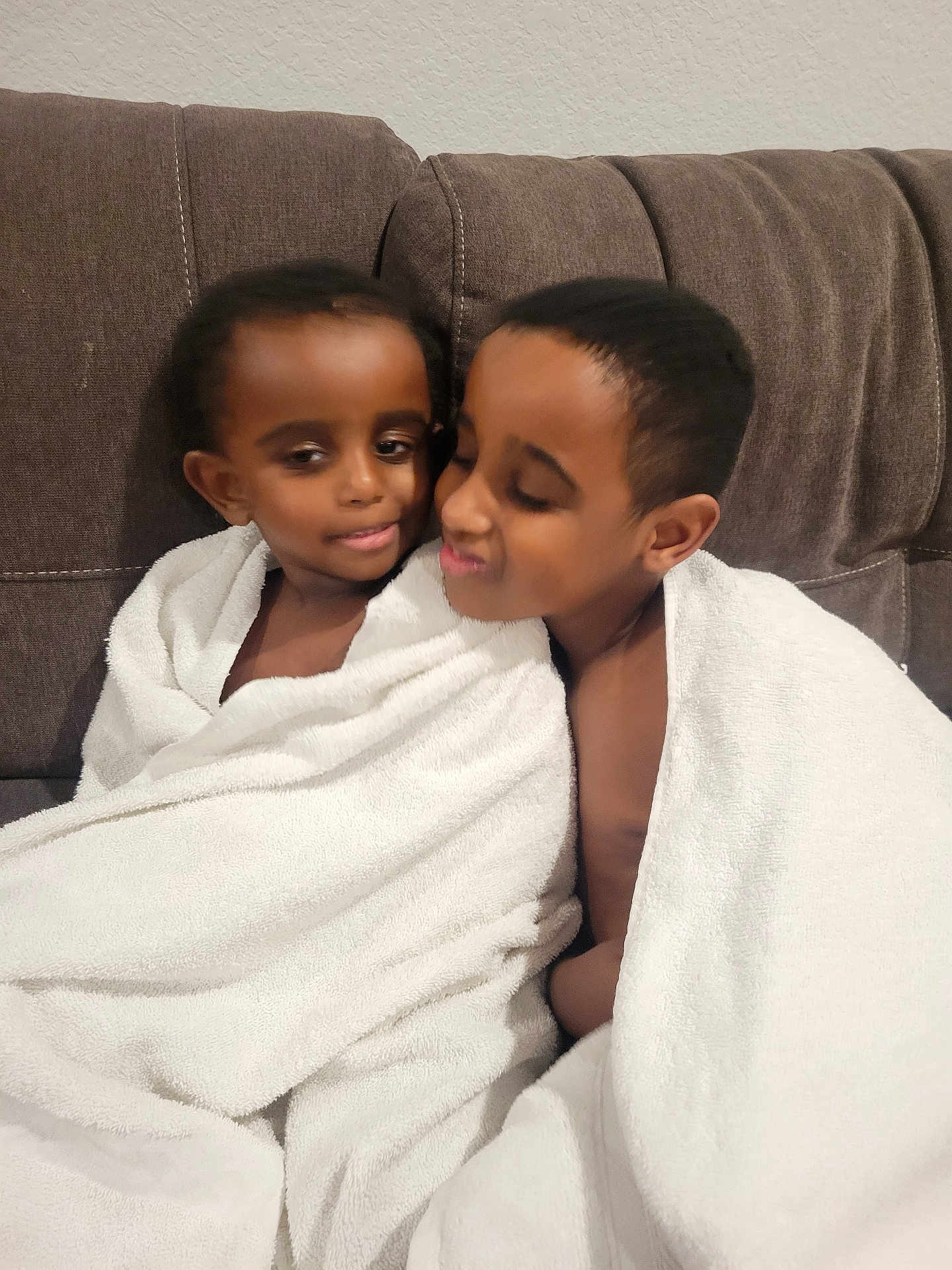 James is registered to the contest to win money with this photo: child, children, towel, white_towel, couch, brown_couch, indoor, portrait, smile, affection, siblings, close, wrapped, cozy, cute, happy, toddler, young, family, love