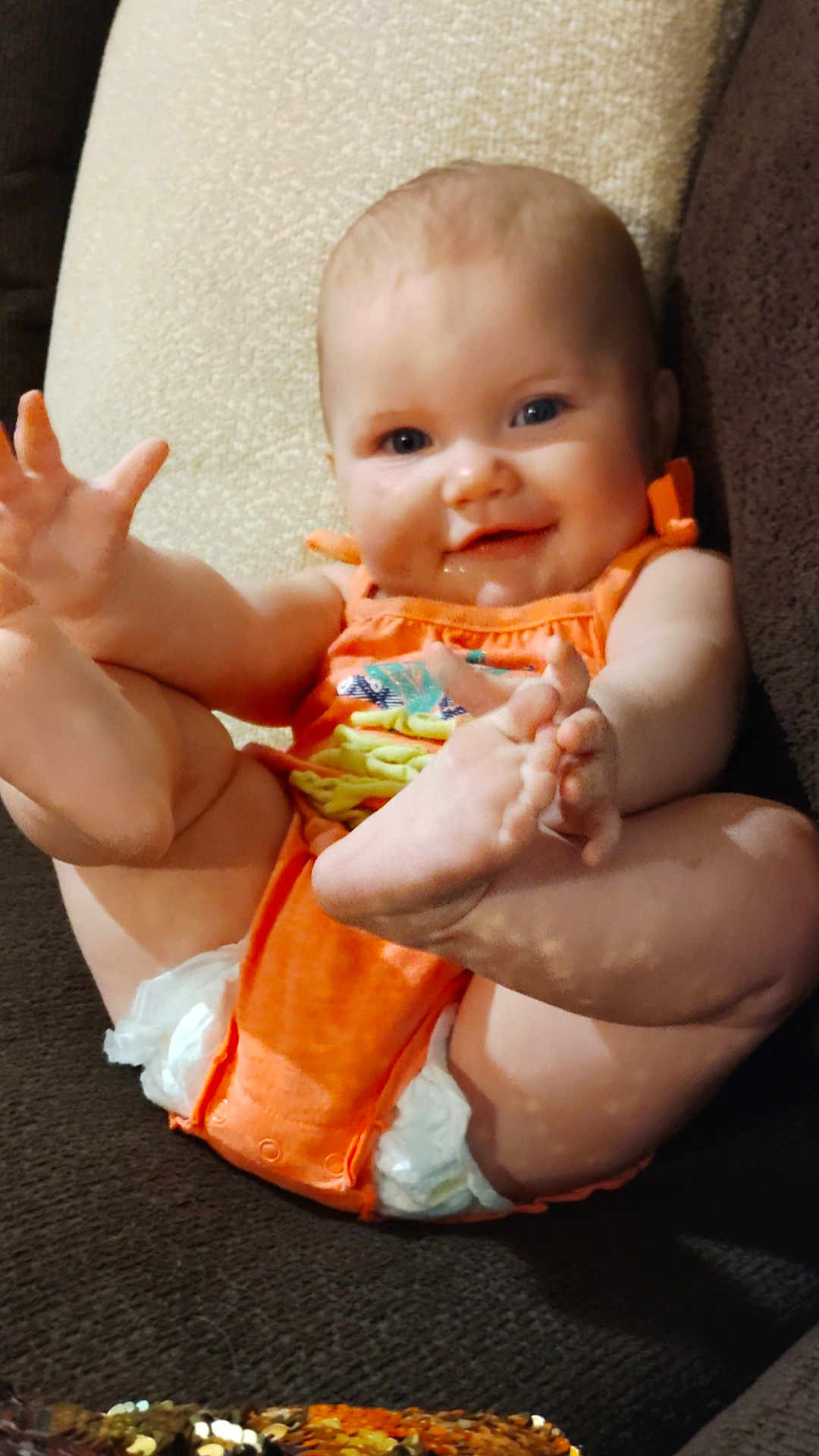 Maci is registered to the contest to win money with this photo: baby, infant, smiling, orange_clothing, diaper, couch, furniture, happy, cute, child, skin, foot, hand, face, indoors, person, sitting, plush, cozy, relaxed