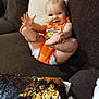 Maci joined the competition — help win amazing prizes! baby, child, smiling, orange_outfit, couch, brown_couch, sequin_pillow, playful, feet, hands, infant, happy, indoor, person, cute, sitting, face, head, comfort, home