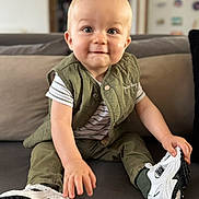 Mathéïs a rejoint le concours — aidez-le/la à gagner de superbes lots ! toddler, child, baby, sitting, couch, shoe, sneaker, green_vest, striped_shirt, indoor, smile, face, hand, footwear, person, home, furniture, cute, young_child, blond_hair