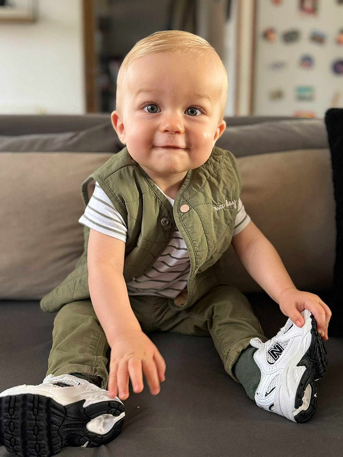 Mathéïs a rejoint le concours — aidez-le/la à gagner de superbes lots ! toddler, child, baby, sitting, couch, shoe, sneaker, green_vest, striped_shirt, indoor, smile, face, hand, footwear, person, home, furniture, cute, young_child, blond_hair