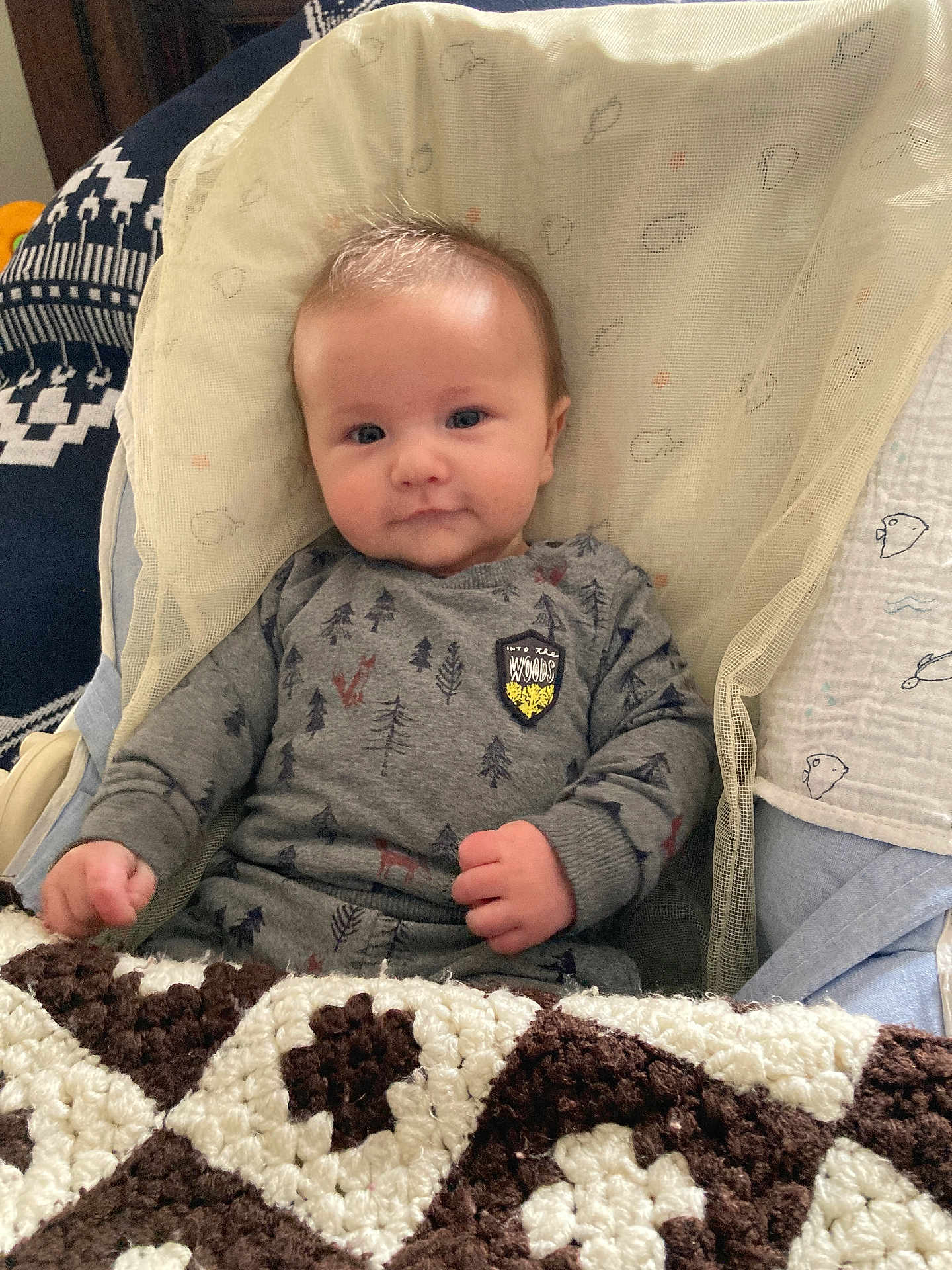 Nolan participe au concours pour gagner de l'argent avec cette photo : baby, infant, child, onesie, grey_clothing, blanket, knitted_blanket, patterned_clothing, indoor, seated, netted_fabric, blue_eyes, cute, portrait, soft_lighting, young_child, baby_face, hand, comfort, smile