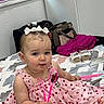 baby, bag, bed, blanket, child, curly_hair, curtain, cute, foot, headband, heart_pattern, holding, indoor, person, pink_dress, portrait, shoes, sitting, smiling, toy