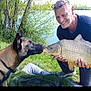 man, dog, fish, lake, grass, trees, outdoor, nature, animal, pet, fishing, water, happy, smiling, catch, friendship, leisure, daylight, collar, kneeling