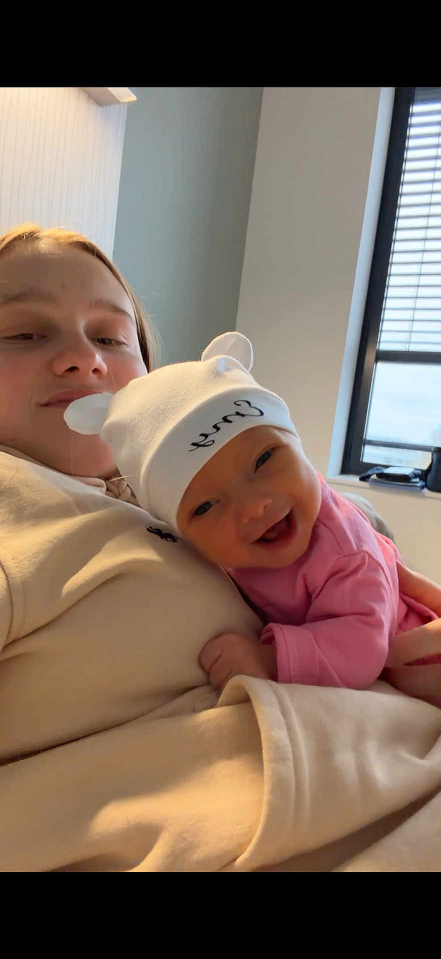 Emy a rejoint le concours — aidez-le/la à gagner de superbes lots ! baby, child, adult, hat, smile, indoor, window, hoodie, person, face, cute, happy, cozy, light, skin, clothing, infant, holding, casual, relaxed