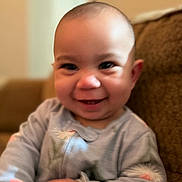 Emma is registered to the contest to win money with this photo: baby, child, infant, smiling, happy, portrait, close_up, face, eyes, laughing, indoors, couch, seated, onesie, clothing, warm_lighting, home, photograph, adorable, head