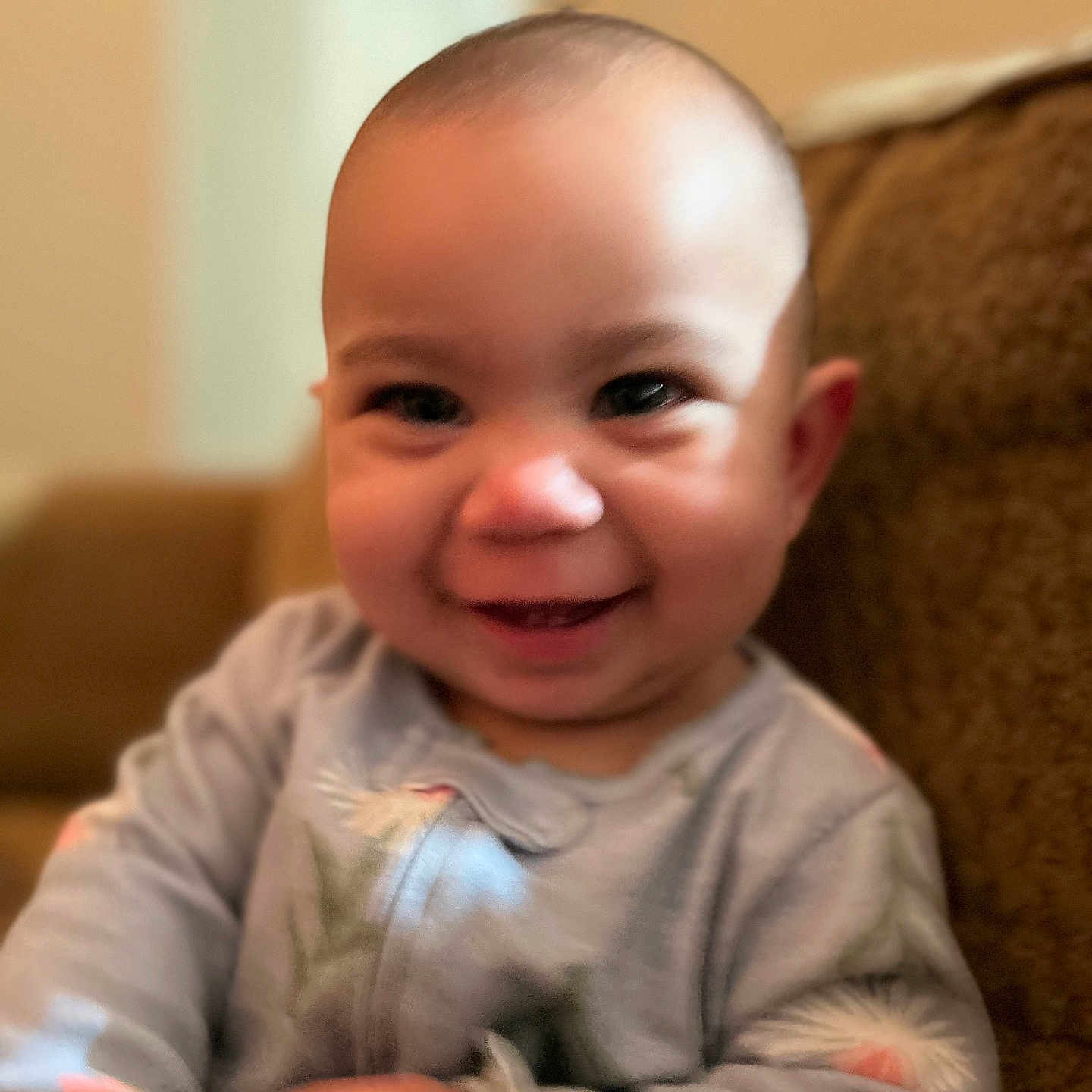 Emma is registered to the contest to win money with this photo: baby, child, infant, smiling, happy, portrait, close_up, face, eyes, laughing, indoors, couch, seated, onesie, clothing, warm_lighting, home, photograph, adorable, head