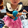 barefoot, bed, black_top, blanket, blue_object, child, clothing, dog, expression, eyes, face, furniture, hand, indoor, minnie_mouse, person, pillow, pink_tutu, room, toddler