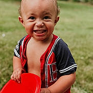 Amir is registered to the contest to win money with this photo: toddler, child, smiling, red_chair, outdoor, grass, happy, boy, short_hair, casual_clothing, portrait, daylight, cute, playful, person, young_child, summer, nature, fun, holding_object