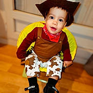 Loüka a rejoint le concours — aidez-le/la à gagner de superbes lots ! baby, child, toddler, cowboy_costume, hat, bandana, brown_clothing, cow_pattern, pants, black_shoes, smile, face, eyes, indoor, wooden_floor, chair, yellow_chair, cute, portrait, happy