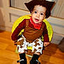 baby, child, toddler, cowboy_costume, hat, bandana, brown_clothing, cow_pattern, pants, black_shoes, smile, face, eyes, indoor, wooden_floor, chair, yellow_chair, cute, portrait, happy