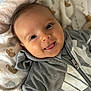baby, child, face, smile, tongue_out, hoodie, gray_clothing, blanket, animal_print, cute, infant, lying_down, happy, closeup, person, soft_texture, cozy, warm, indoor, portrait