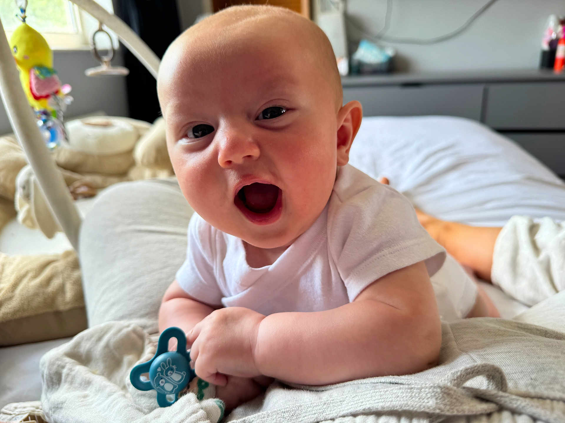 Harley joined the competition — help win amazing prizes! baby, infant, pacifier, white_clothing, bed, blanket, smiling, happy, face, indoors, toy, cute, skin, person, head, mouth_open, lying_down, soft_light, home, comfort