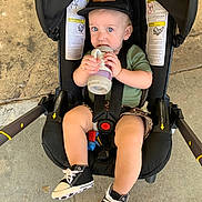 Myles joined the competition — help win amazing prizes! toddler, child, baby, stroller, sippy_cup, hat, cap, black_shoes, sneakers, concrete_floor, child_seat, sitting, straps, clothing, person, footwear, outdoor, expression, hydration, casual