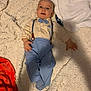 baby, blue_bow_tie, suspenders, blue_pants, striped_socks, blanket, textured_blanket, remote_control, infant, lying_down, indoor, cute, clothing, face, head, hand, footwear, expression, home, child