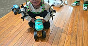Shavena joined the competition — help win amazing prizes! child, toddler, toy, toy_truck, wooden_floor, indoor, beads, hair_accessory, crouching, curious, clothing, sneakers, person, flooring, furniture, living_room, play, kid, cute, home