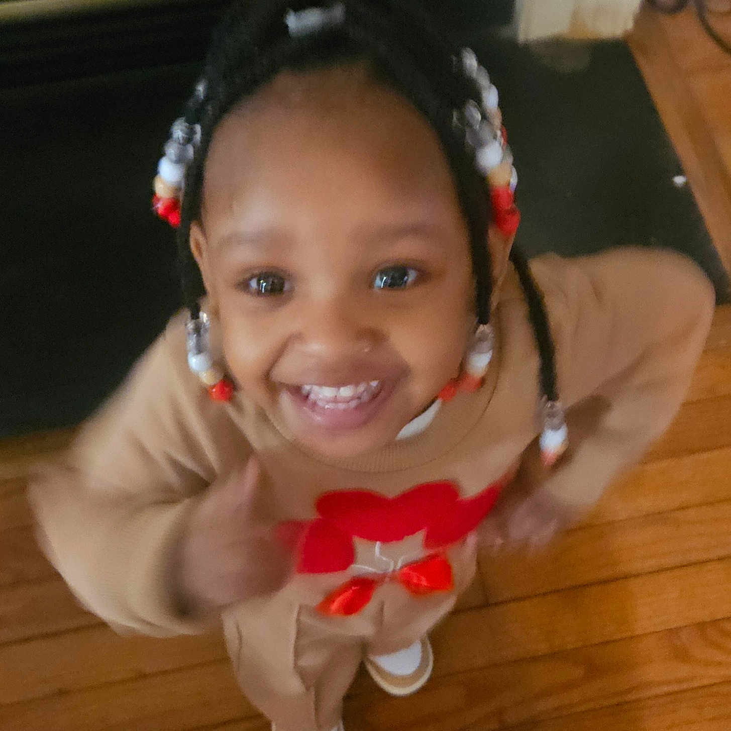 Shavena is registered to the contest to win money with this photo: toddler, child, smile, indoor, wooden_floor, beads, braids, happy, thumbs_up, clothing, person, face, young_child, hair_accessories, casual_wear, cheerful, portrait, cute, playful, home