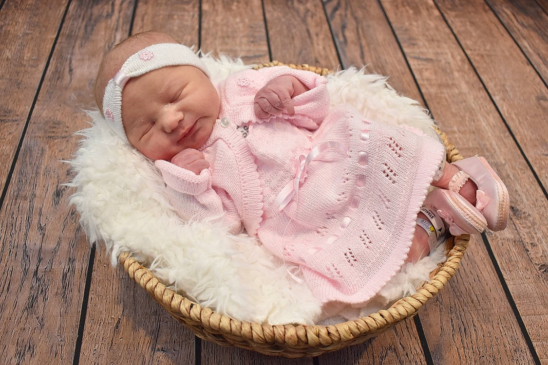 Evelyn is registered to the contest to win money with this photo: baby, baby_products, baby_sleeping, baby_toddler_clothing, basket, cheek, comfort, fashion_accessory, fur, grass, hair_accessory, hardwood, headwear, infant_bed, linens, peach, person, pink, sitting, tableware