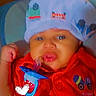 Loyal joined the competition — help win amazing prizes! baby, infant, hat, red_clothing, toy, pacifier, face, child, indoor, closeup, expression, sitting, cute, person, headwear, time_stamp, text_overlay, hand, blue, colorful