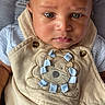 baby, infant, child, face, eyes, clothing, overalls, lion_patch, serious_expression, blue_shirt, blanket, pattern, cute, indoors, portrait, closeup, soft_surface, skin, head, person