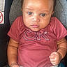 baby, infant, car_seat, clothing, maroon_shirt, logo, pants, person, child, indoor, seat, cute, portrait, young, small_hands, looking_up, casual_wear, light_skin, short_hair, serious_expression