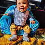 armchair, baby, bib, blanket, blue_armchair, carpet, child, curly_hair, cute, eyes, face, hands, infant, living_room, portrait, seated, smiling, socks, tv_screen, yellow_pants