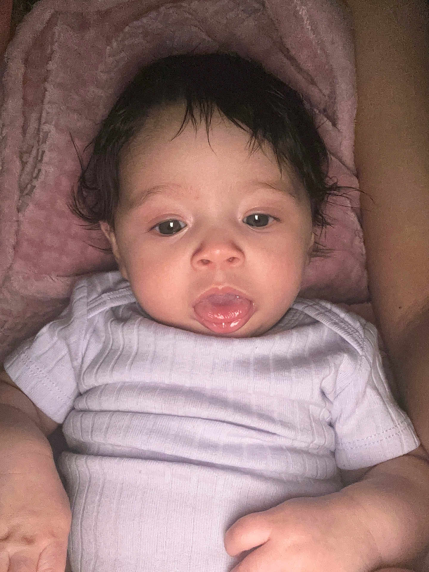 Amora is registered to the contest to win money with this photo: baby, infant, tongue, white_onesie, pink_blanket, wet_hair, closeup, face, skin, hand, arm, lying_down, cute, expression, child, young, indoors, soft_texture, person, portrait