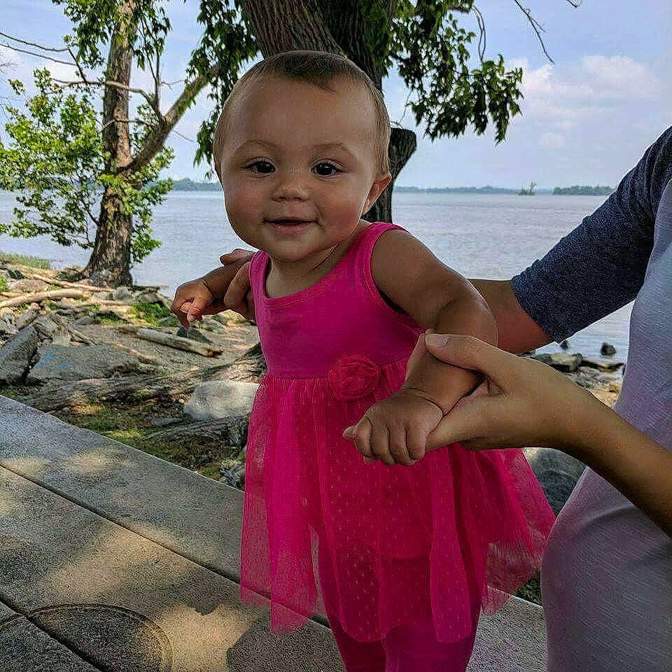 Milani is registered to the contest to win money with this photo: baby_toddler_clothing, dress, face, facial_expression, fun, gesture, grass, hairstyle, happy, human, joy, leisure, mammal, person, shoulder, skin, sky, smile, toddler, travel