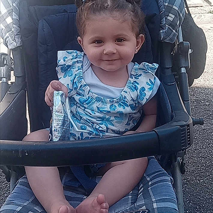 Assïya a rejoint le concours — aidez-le/la à gagner de superbes lots ! baby, baby_clothing, barefoot, blue_dress, child, cute, daylight, fabric, hair_buns, happy, infant, outdoor, person, portrait, seatbelt, smile, snack, stroller, sunlight, toddler