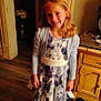 black_shoes, blonde_hair, cabinet, casual_clothing, child, cozy, dress, floral_pattern, furniture, girl, happy, home, indoor, long_hair, person, portrait, smiling, standing, white_tights, wooden_floor