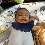 Jayce joined the competition — help win amazing prizes! baby, infant, child, smiling, happy, portrait, face, eyes, curly_hair, lying_down, bib, clothing, blanket, stuffed_toy, play_mat, indoor, close_up, baby_bedding, cozy, photography