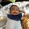 baby, infant, child, smiling, happy, portrait, face, eyes, curly_hair, lying_down, bib, clothing, blanket, stuffed_toy, play_mat, indoor, close_up, baby_bedding, cozy, photography