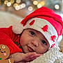 baby, infant, christmas_hat, red_clothing, holiday, festive, face, cute, smiling, indoors, soft_blanket, decorations, cartoon_gingerbread, cartoon_snowman, winter, closeup, portrait, holiday_season, celebration, child