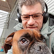Marley a rejoint le concours — aidez-le/la à gagner de superbes lots ! man, dog, selfie, glasses, headphones, brown_dog, close_up, portrait, indoor, smile, facial_hair, casual_clothing, canine, pet, companion, headshot, friendly, indoor_lighting, human, animal