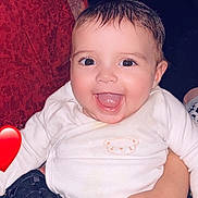 Djennah a rejoint le concours — aidez-le/la à gagner de superbes lots ! baby, infant, child, smiling, happy, face, eyes, tongue, onesie, white_clothing, short_hair, wet_hair, cheeks, arm, hand, red_heart, pillow, blanket, indoor, portrait