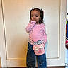 Arabella is registered to the contest to win money with this photo: child, girl, portrait, standing, indoors, hallway, pink_shirt, pigtails, hair_bows, smiling, hand_on_face, purse, bow_purse, jeans, wide_leg_pants, shoes, wood_floor, door, home, fashion