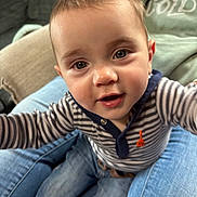 Flint is registered to the contest to win money with this photo: baby, child, cute, smiling, striped_shirt, jeans, person, indoors, living_room, close_up, face, eyes, hands, happy, casual_clothing, seated, affectionate, family, home, curious