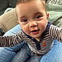 baby, child, cute, smiling, striped_shirt, jeans, person, indoors, living_room, close_up, face, eyes, hands, happy, casual_clothing, seated, affectionate, family, home, curious