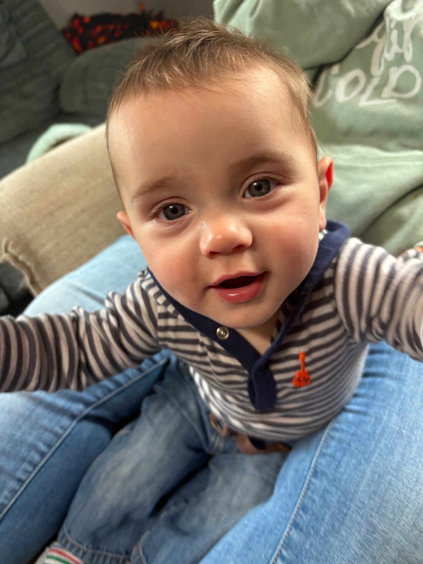 Flint is registered to the contest to win money with this photo: baby, child, cute, smiling, striped_shirt, jeans, person, indoors, living_room, close_up, face, eyes, hands, happy, casual_clothing, seated, affectionate, family, home, curious