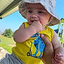 baby, blue_dinosaur, bucket_hat, casual_clothing, child, cute, dinosaur, fingers, green_grass, hand, hat, holding, outdoor, person, playground, scooter_graphic, smiling, summer, sunny, yellow_tank_top