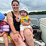 Flint is registered to the contest to win money with this photo: woman, baby, child, boat, lake, water, cloudy_sky, hat, yellow_shirt, floaties, smile, happy, outdoor, nature, summer, family, people, sitting, casual, relaxation