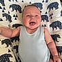 baby, infant, smiling, tongue_out, onesie, cushion, bear_pattern, blue_clothing, happy, cute, child, indoors, soft_fabric, playful, person, portrait, young_child, closeup, cheerful, resting
