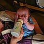 baby, bottle, feeding, blanket, striped_clothing, hands, adult_hand, indoor, table, paper_plate, cup, person, child, newborn, care, comfort, rest, holding, toddler, family