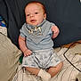 baby, infant, blue_clothing, bib, giraffe_print, socks, bed, blanket, striped_blanket, cute, child, person, indoor, lying_down, soft_lighting, newborn, resting, small_hands, small_feet, comfort