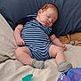 baby, sleeping, onesie, striped_clothing, bed, pillow, blanket, pacifier, sock, infant, cute, resting, soft_fabric, child, indoor, comfort, relaxation, face, head, peaceful
