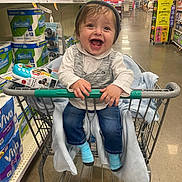 Isaac joined the competition — help win amazing prizes! toddler, shopping_cart, grocery_store, child, happy, smiling, clothing, toy, beanie, socks, jeans, blanket, aisle, packaging, paper_towels, floor, metal, handle, person, indoor