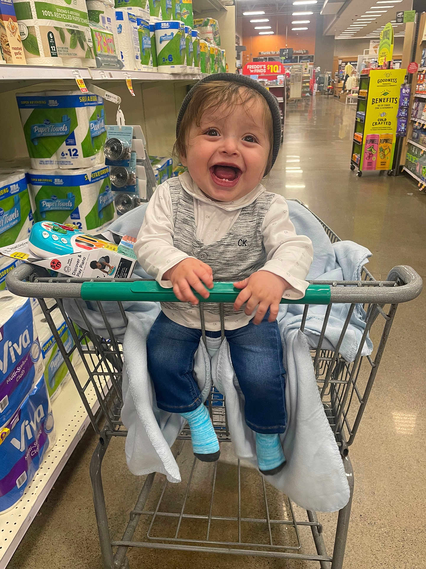 Isaac joined the competition — help win amazing prizes! toddler, shopping_cart, grocery_store, child, happy, smiling, clothing, toy, beanie, socks, jeans, blanket, aisle, packaging, paper_towels, floor, metal, handle, person, indoor