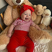 Robyn joined the competition — help win amazing prizes! baby, child, teddy_bear, stuffed_animal, plush, red_clothing, striped_shirt, headband, smiling, indoors, bed, blanket, cozy, cute, happy, person, toy, soft, sitting, comfort